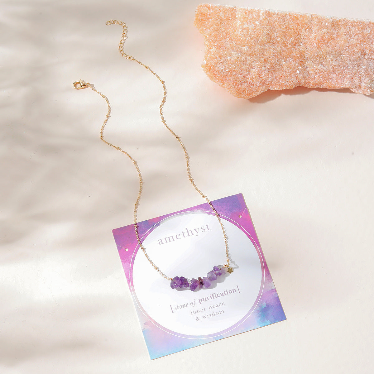 "Top flat-lay view of a delicate gold amethyst necklace with raw gemstone beads, presented on a card highlighting amethyst as the stone of purification, inner peace, and wisdom. The necklace chain is beautifully displayed in a curved pattern, showcasing its elegant design by Oyracha Jewelry."