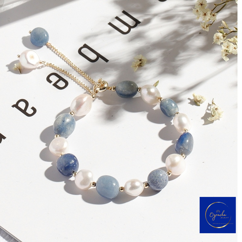 Angled top view of a moonstone and pearl bracelet by Oyracha Jewelry, featuring natural blue moonstone and freshwater pearls with gold accents, elegantly displayed in soft lighting. This delicate bracelet highlights a blend of calming blue and white tones, perfect for everyday elegance or special occasions