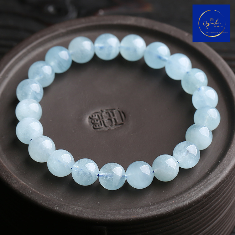 Top view of a smooth aquamarine bead bracelet, elegantly placed on a round, engraved surface. This calming aquamarine bracelet from Oyracha Jewelry showcases the soothing blue tones of natural stones, ideal for promoting inner peace and serenity.