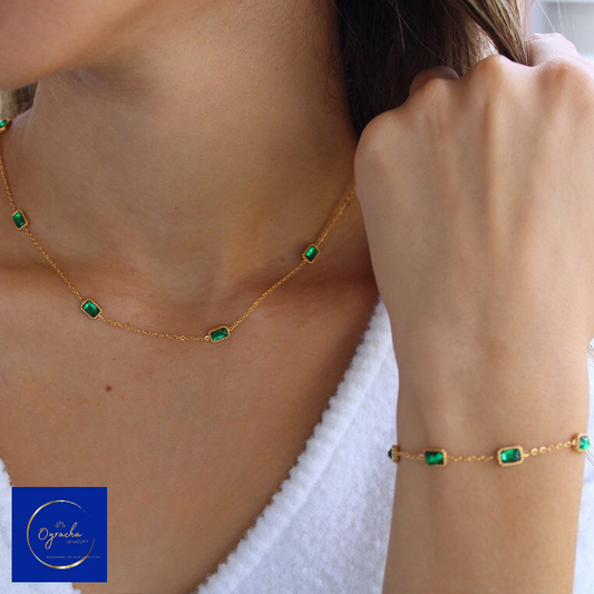 Close-up side view of a woman wearing an elegant emerald gemstone necklace and matching bracelet from Oyracha Jewelry. The gold chain is delicately adorned with rectangular green emerald stones, creating a sophisticated and timeless look. The photo highlights the minimalistic and refined design, perfect for adding a touch of luxury to any outfit.