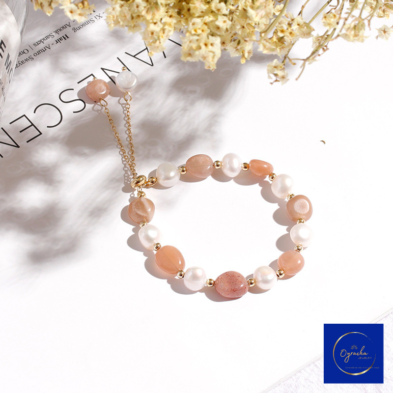 Top angled view of a peach moonstone and freshwater pearl bracelet by Oyracha Jewelry, featuring soft peach-colored moonstones paired with radiant pearls and gold bead accents. The bracelet is elegantly laid on a white background with floral decor, highlighting its luxurious and delicate craftsmanship.